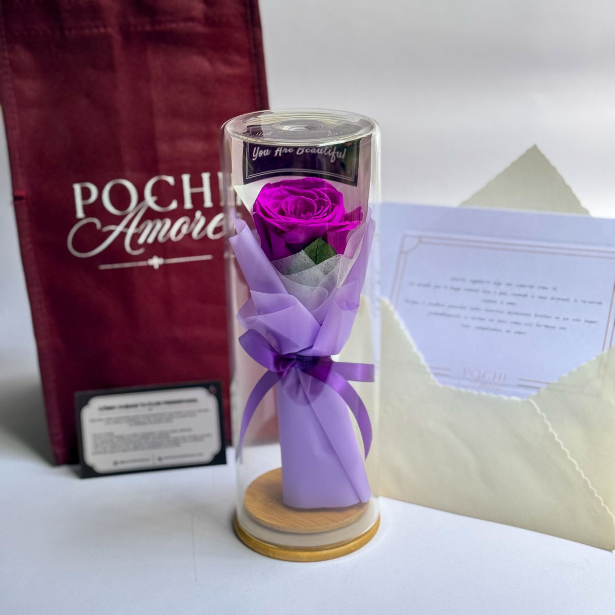 Rosa Eterna Elegance morada en tubo de vidrio junto a bolsa de regalo Pochi Amore