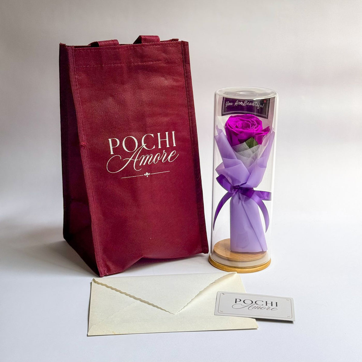 Rosa Eterna Elegance morada en tubo de vidrio junto a bolsa granate